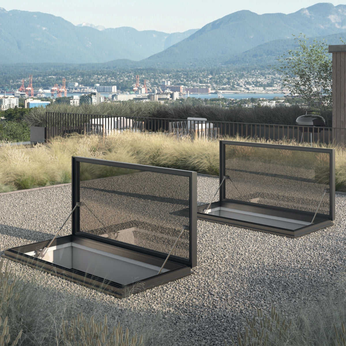 Two black metal mesh skylight vent panels installed on a gravel roof terrace, with a mountainous city landscape in the background.